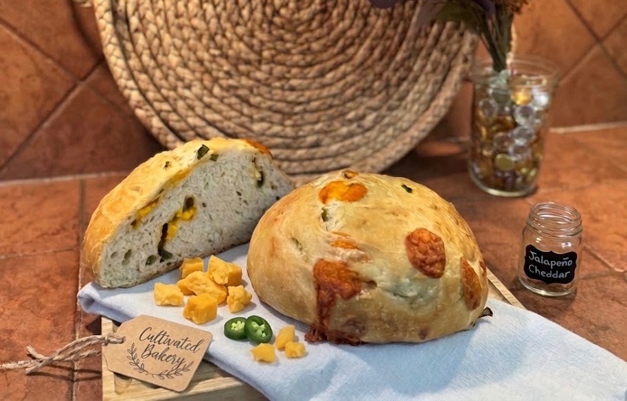 Jalapeño cheddar sourdough cut open beside a wheel of the loaf