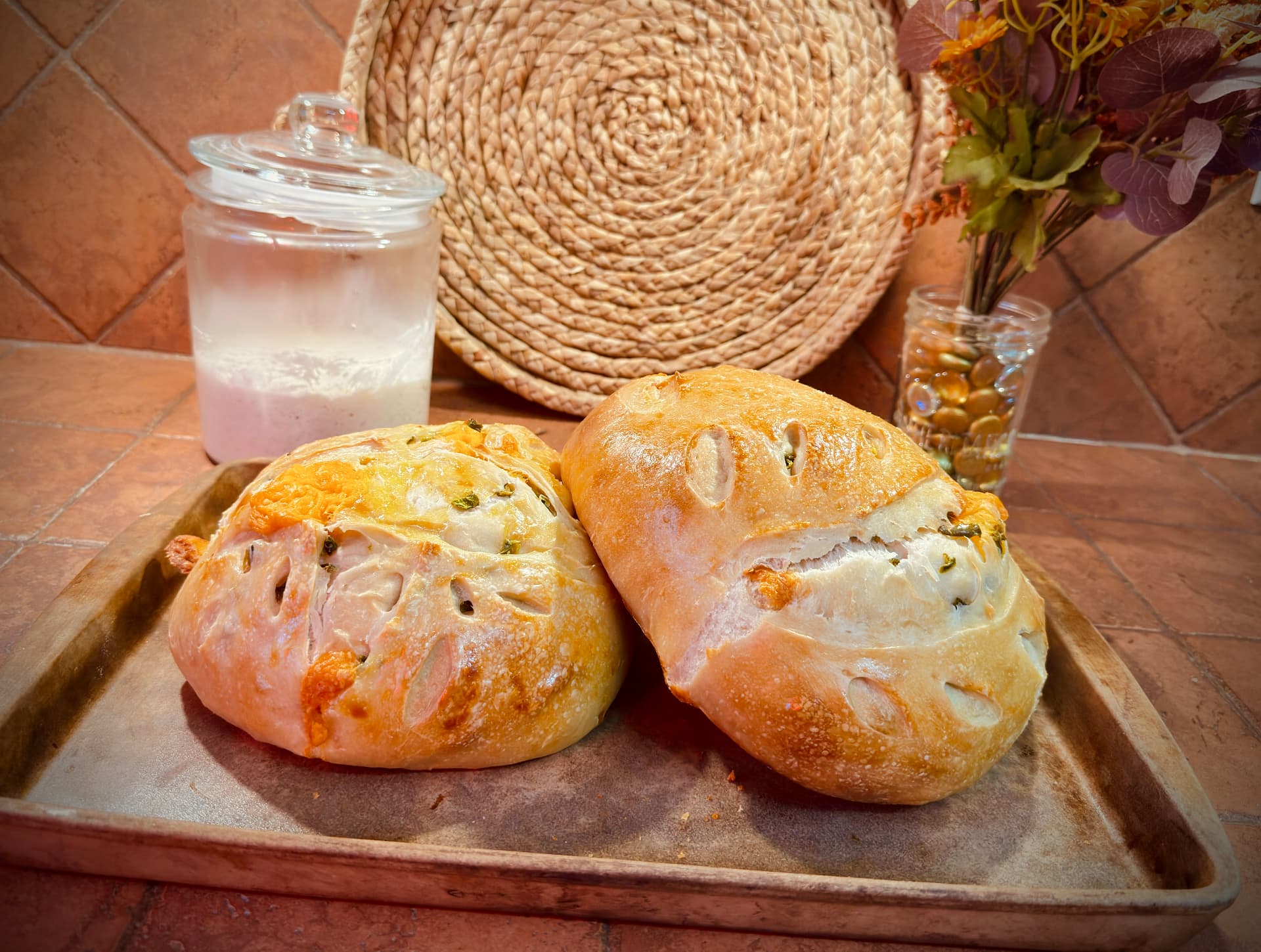 Two jalapeño cheddar sourdough boules fresh from the oven on a worn baking tray